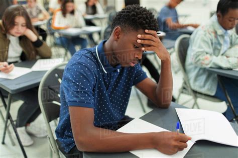 Focused High School Boy Taking Exam At Desk In Classroom Stock Photo
