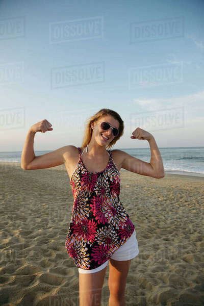 Smiling Caucasian Teenage Girl Flexing Biceps On Beach Stock Photo