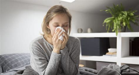 Sick Woman Sitting In Bed Blowing Nose With Napkin