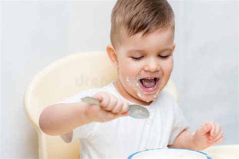 Adorable Baby Boy Eats Porridge With A Small Spoon Himself Stock Photo