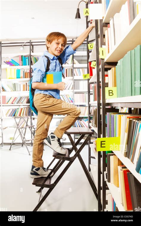 Boy Climbing On Step Ladder In Library Stock Photo Alamy
