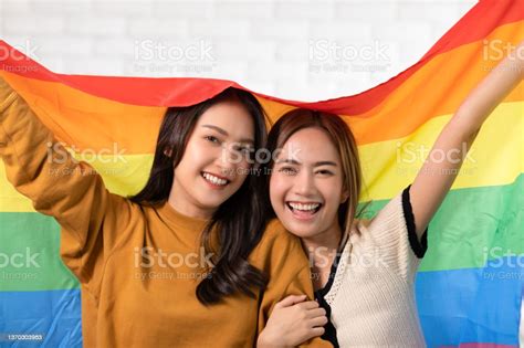 foto de casal jovem lésbica lgbtq asiático sorrindo segurando a bandeira do orgulho felicidade