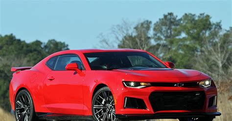 A Red Chevrolet Camaro Is Driving Down The Road