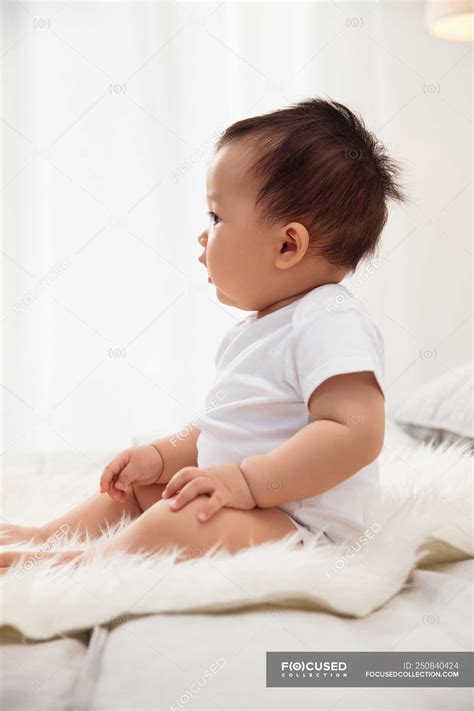 Side View Of Adorable Asian Baby Sitting On Bed At Home — Beautiful