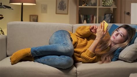 Tired Woman Texting On Smartphone While Lying On A Sofa In The Living