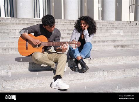 A Young Latin Couple In Love Playing The Guitar And Singing Sitting On