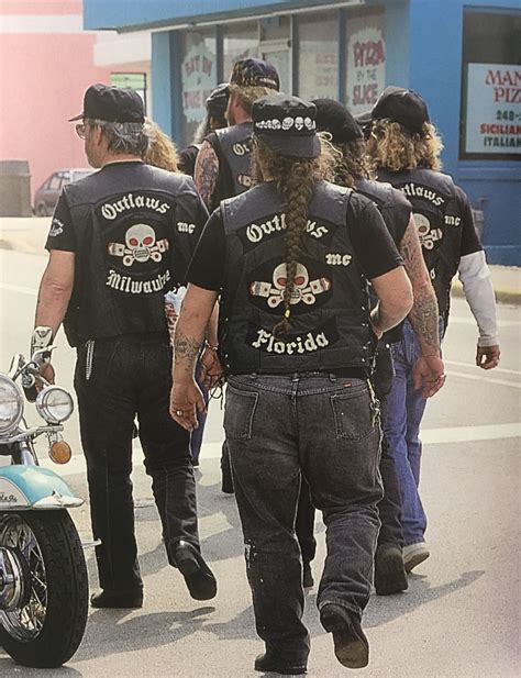 A Group Of Bikers Are Walking Down The Street In Front Of A Motorcycle Shop