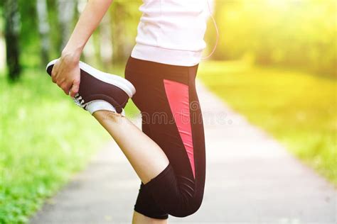 Young Fitness Woman Runner Stretching Legs Before Run On Grass Stock