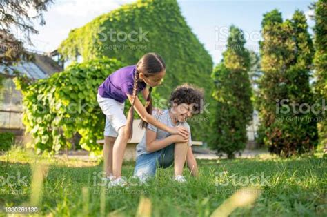 Girl Bending Over To Boy Sitting On Grass Stock Photo Download Image