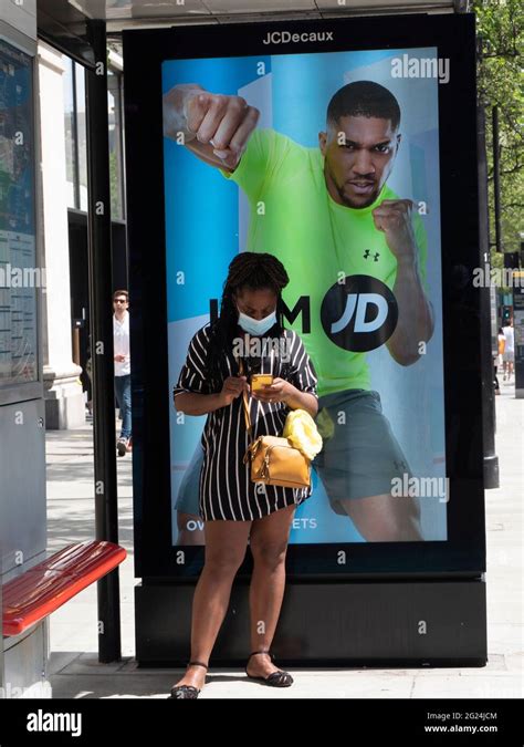 female on phone in oxford street stands at bus stop in front of jcdecaux outdoor advert for jd