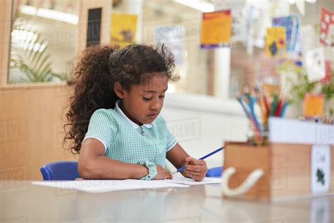 Schoolgirl Writing At Classroom Desk In Primary School Stock Photo