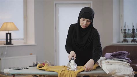 Diligent Muslim Housewife In Black Hijab Ironing Yellow Sweater At Home