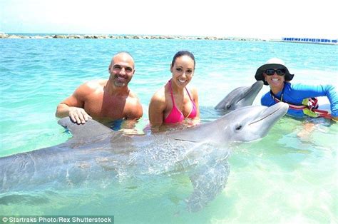 Two Women And A Man In The Water With A Large Dolphin That Is Smiling