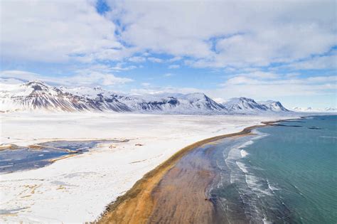 Aerial View Of Beach Along Land And Mountains Covered With Snow During