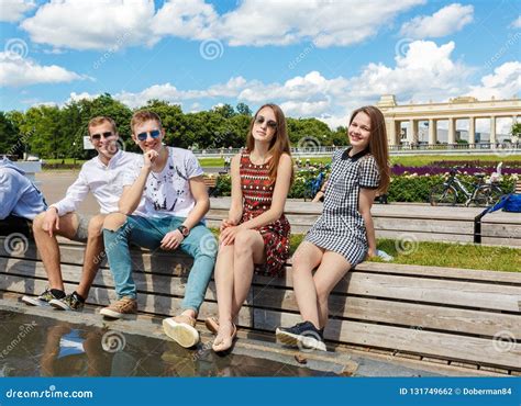 Group Of Young Friends Sitting On A Park Bench Talking Stock Photo