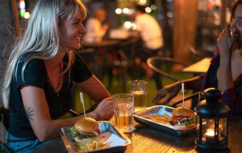 girlfriends eating burgers in a street restaurant at night by stocksy contributor jovo