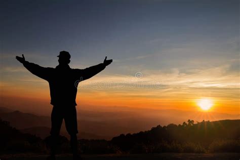 Silhouette Of Man Standing On Top Of Mountain With Hands Raised Up On