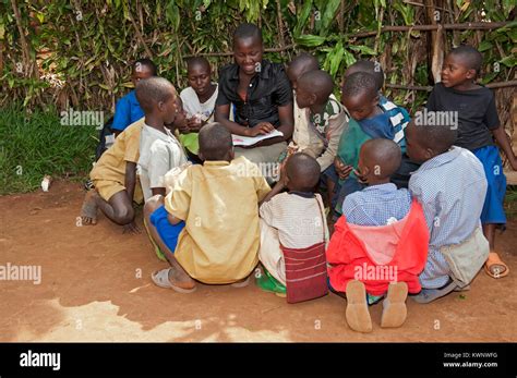 Young Teacher Reading A Story To Children Gathered Around Her Rwanda
