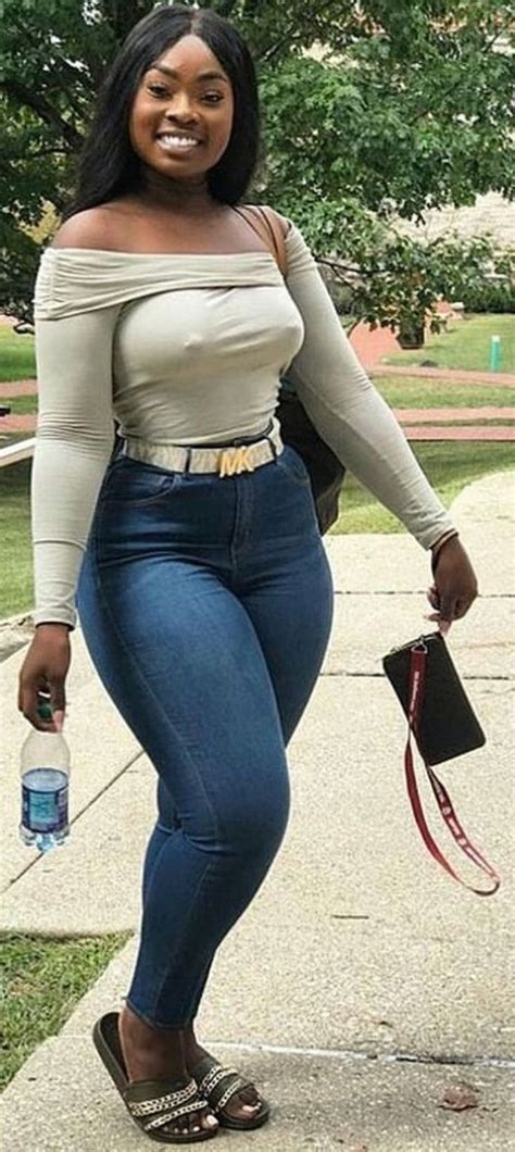 a woman in high waist jeans is smiling and holding a water bottle while standing on the sidewalk