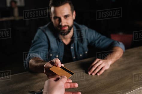 Cropped Image Of Visitor Sitting At Bar Counter And Giving Credit Card To Bartender Stock