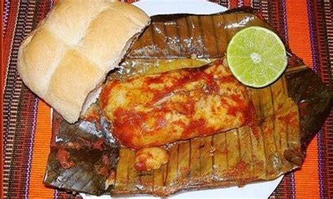 A White Plate Topped With Meat And Cheese Covered Enchilada Next To A Roll