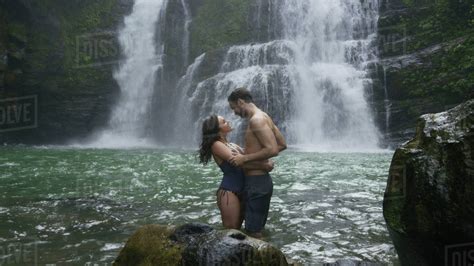 Romantic Couple Hugging In River Under Tropical Waterfall Stock Photo