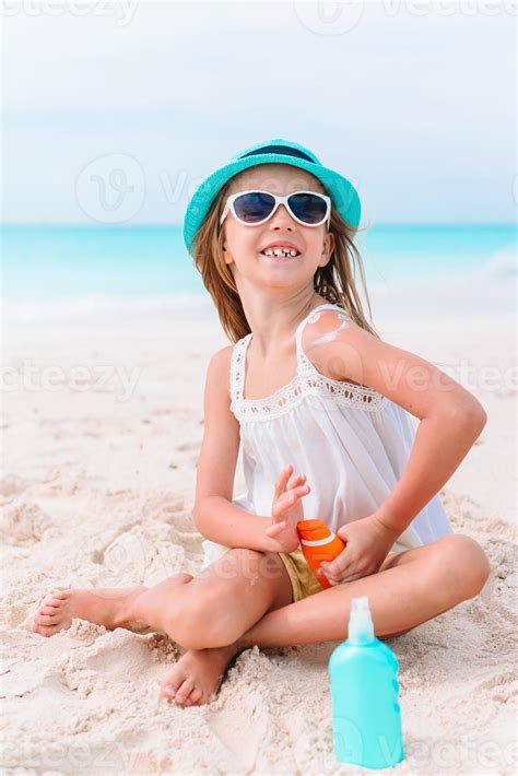 Little Girl With Bottle Of Sun Cream Sitting At Tropical Beach 18040585