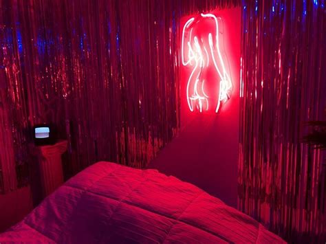 A Red Neon Sign In The Corner Of A Room Next To A Bed With A Pink Comforter
