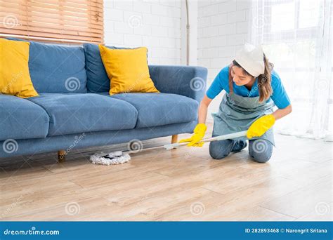 empregada doméstica asiática ou empregada doméstica usa esfregão para limpar debaixo do sofá na