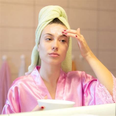 A Woman Applies Face Cream While Looking In A Mirror Homemade Face Care Face Scrub Homemade