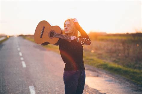 Beautiful Young Woman Strolling In Field With Guitar Over Her Shoulder By Stocksy Contributor