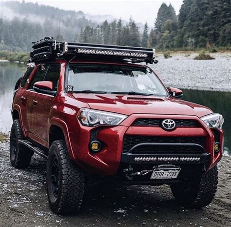 A Red Toyota 4runner Parked On The Side Of A River With Mountains In