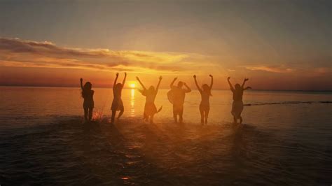Group Of Happy Friends Running In To Water At Sunset Silhouettes Of
