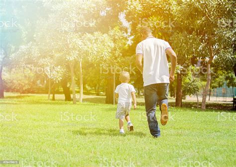 Father And Son Running And Chasing Each Other In Park Stock Photo