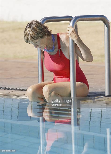 Mature Woman Sitting At Edge Of Swimming Pool Wearing Swimsuit Foto De