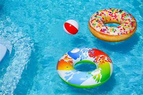 Bright Inflatable Rings And Beach Ball Floating In Swimming Pool On