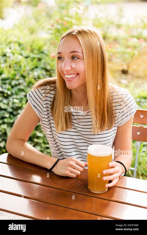 Positive Young Blond Haired Female In Casual Outfit Sitting At Wooden