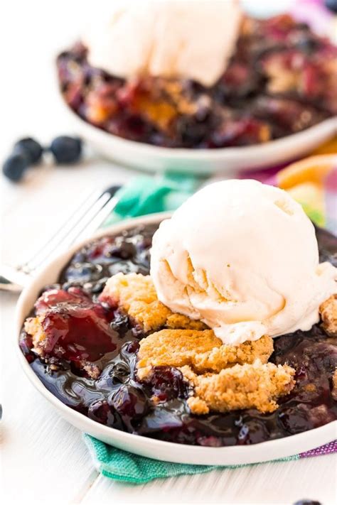 blueberry cobbler with ice cream on top in a white bowl next to another dish