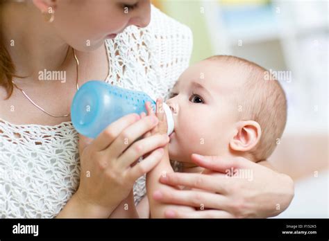 Young Mother At Home Feeding Baby With Milk Bottle Feeling Proud Stock