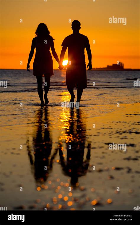 Young Couple Walking A Beach At Sunset Or Sunrise Stock Photo Alamy