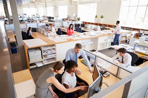 Colleagues Working At A Womans Workstation In A Busy Office North