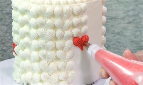 Someone Is Decorating A Cake With White Icing And Red Decorations On