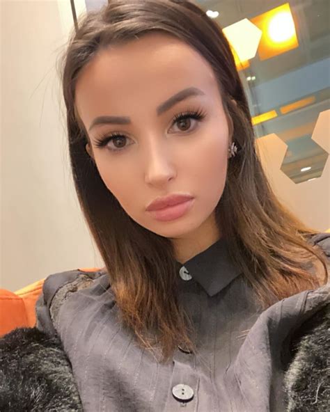 A Woman With Long Brown Hair Wearing A Gray Shirt And Silver Earrings Looking At The Camera