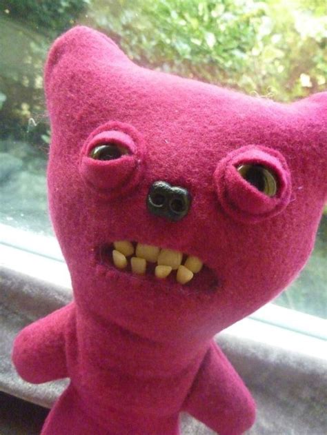 A Pink Stuffed Animal With Big Eyes And Teeth Is Shown In Front Of A Window