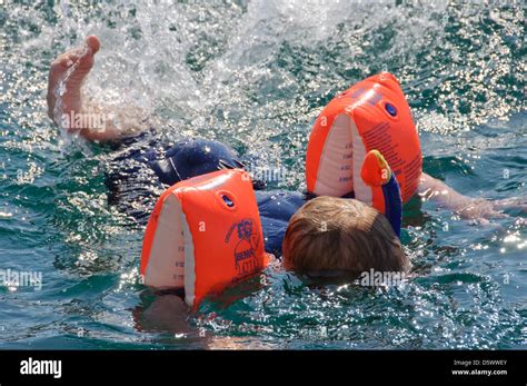Little Caucasian Blond Boy Swims In The Ocean Sea Wearing Floaties