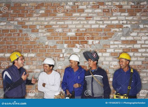 Group Of Laughing Construction Workers By Brick Wall Stock Photo
