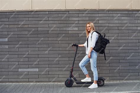 Premium Photo Against Grey Wall Beautiful Blonde In Casual Clothes Riding Electric Schooter