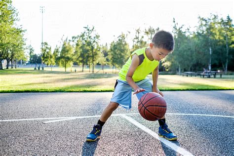 Asian Kid Dribbling A Basketball In An Outdoor Basketball Court By