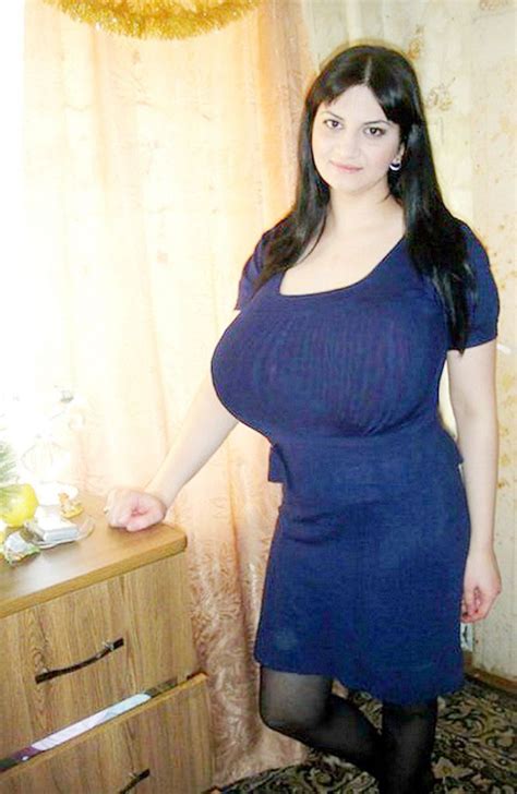 A Woman In A Blue Dress Is Standing Near A Dresser With Glasses On It And Looking At The Camera