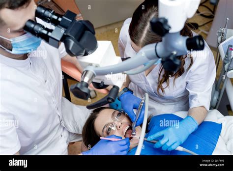Dentist With Assistant Under Microscope Treats The Patients Teeth